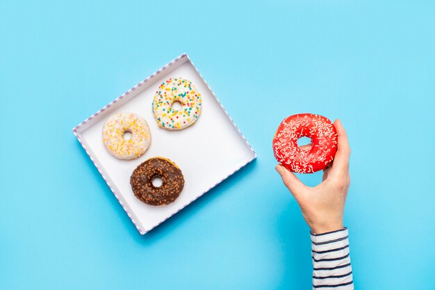 Feminino mão segura uma rosquinha em um azul. Loja de confeitaria conceito, bolos, café.