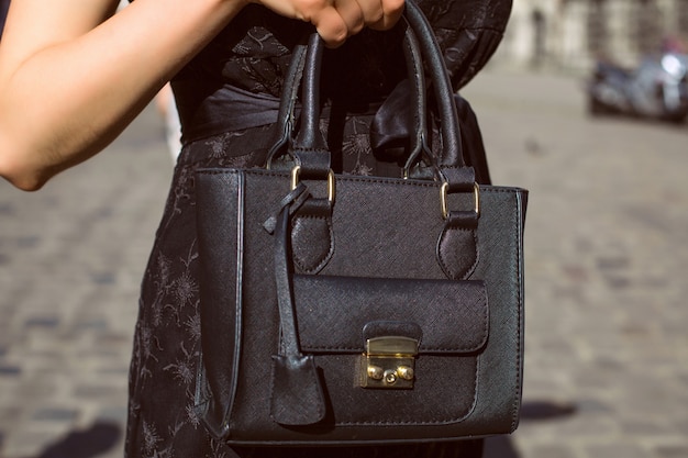 Feminino mão segurando a bolsa de couro preto ao fundo da cidade. Foto de close