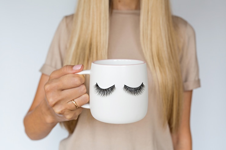 Foto feminino mão segurando a taça com cílios postiços.