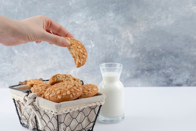 Feminino mão segurando o biscoito de aveia com sementes de gergelim em uma mesa branca.