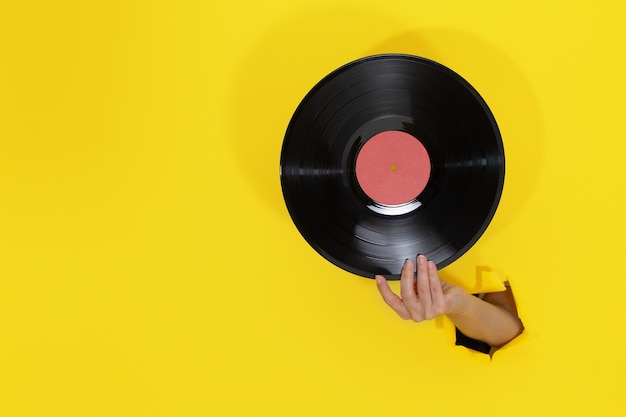 Feminino mão segurando o disco de vinil através do buraco rasgado na parede de papel amarelo. Conceito retrô minimalista