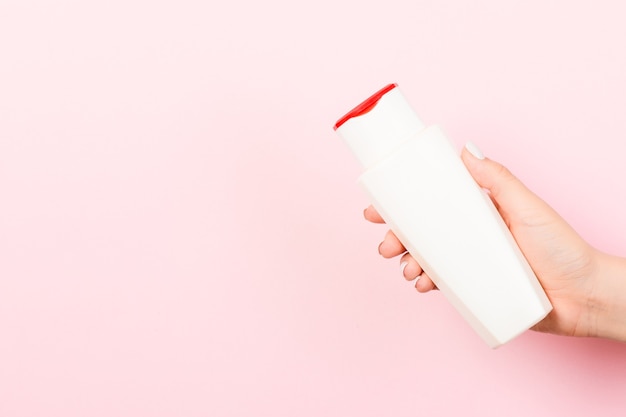 Feminino mão segurando o frasco de cosméticos no fundo rosa com espaço vazio para seu projeto.