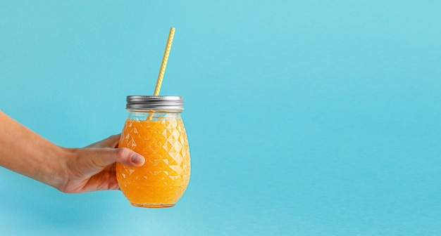 Feminino mão segurando o frasco de suco fresco sobre fundo azul. Uma alimentação saudável, copie o espaço.