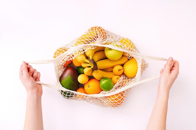 Feminino mão segurando o saco de malha eco com frutas sobre fundo claro. Alimentação saudável e limpa. Conceito de compra ecológica.