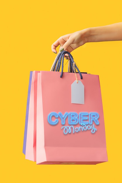 Feminino mão segurando sacolas de compras brilhantes em amarelo. Cyber segunda-feira e conceito de venda