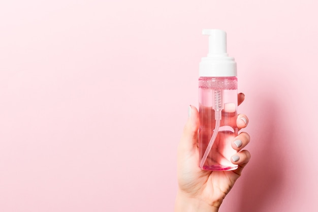Feminino mão segurando spray de cosméticos no fundo rosa com espaço vazio para seu projeto.