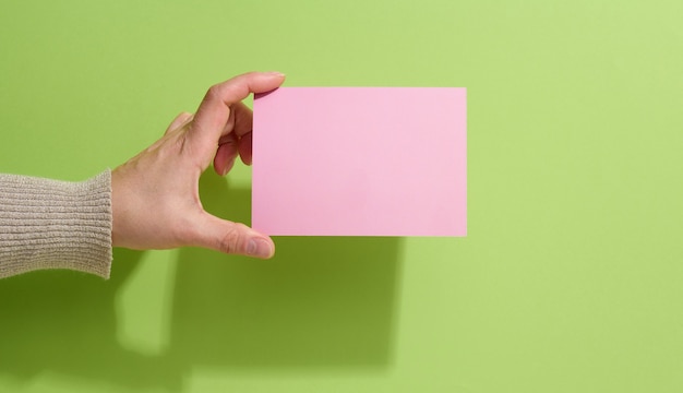 Feminino mão segurando um papel rosa vazio sobre um fundo verde. copiar e colar imagem ou texto, close-up