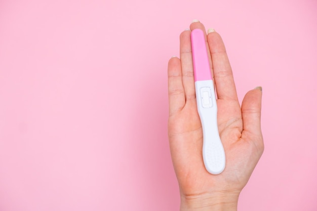 Feminino mão segurando um teste de gravidez no fundo rosa
