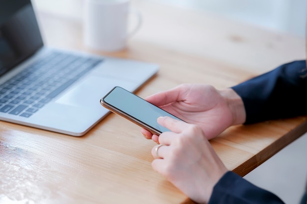 Feminino mão usando smartphone com tela em branco no escritório.