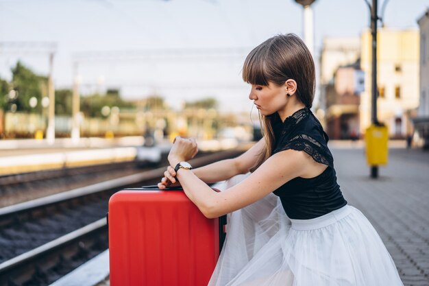 Feminino viajante com mala vermelha esperando trem na estação ferroviária
