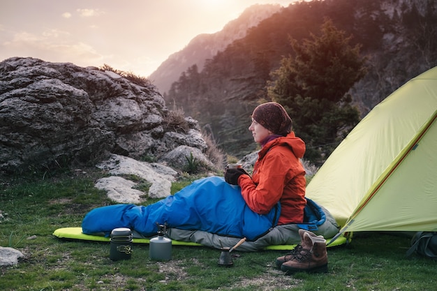 Feminino viajante em um saco de dormir perto da tenda nas montanhas, Turquia