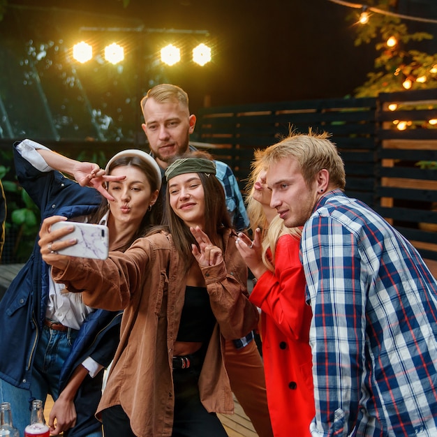 Femininos e masculinos amigos comemorando a festa ao ar livre e fazendo selfies foto no smartphone.