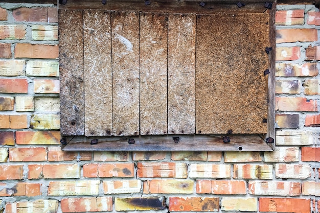 Fenster in verlassener alter Backsteinmauer in Scheune oder geschlossenem altem Haus vernagelt. Nahansicht. Draußen.