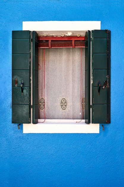 Fenster mit geöffnetem grünem Fensterladen auf blauer Wand. Italien, Venedig, Burano Insel.