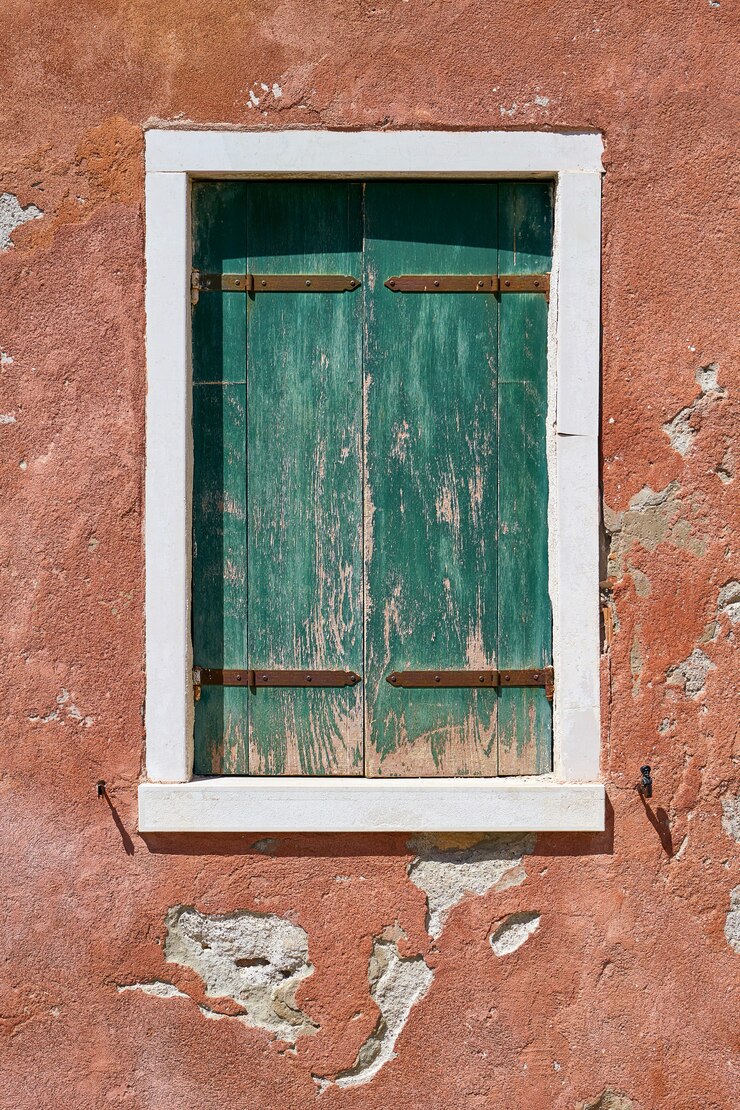 Fenster mit geschlossenem alten grünen grünen Verschluss auf roter Wand. Italien, Venedig, Insel Burano.