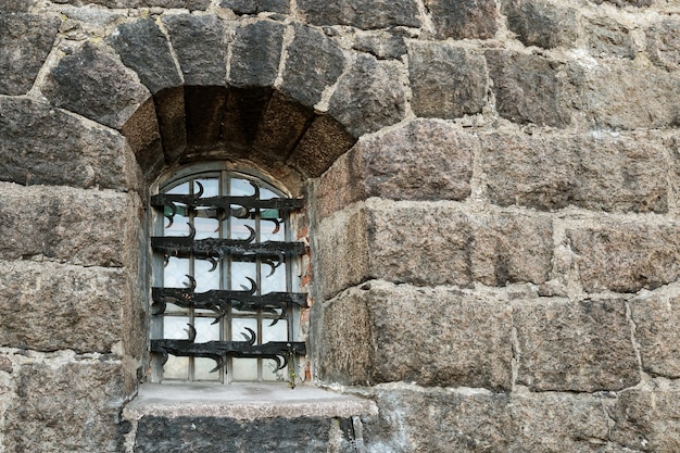 Fenster mit schmiedeeisernem Gitter auf dunkler Steinmauer