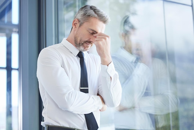 Fenstergeschäftsmann und Stress mit Kopfschmerzen Burnout und überarbeitet im Büro Älterer männlicher Unternehmer und CEO frustriert die psychische Gesundheit und Führungskraft mit Depressionsschmerzen und müde am Arbeitsplatz