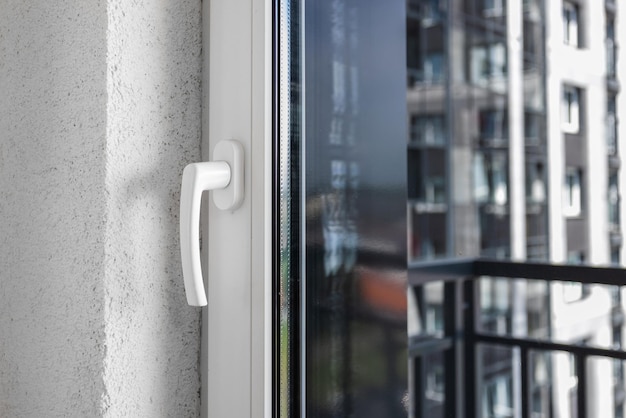 Fensterrahmen aus weißem Metallkunststoff mit einem Griff und Glas, durch die Fenster eines Wohnhauses