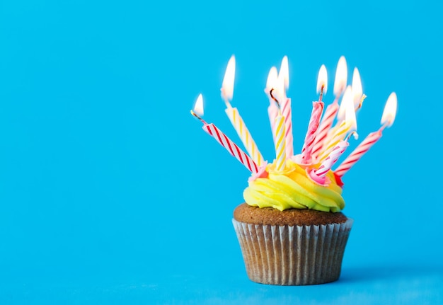 feriado, celebração, saudação e conceito de festa - cupcake de aniversário com muitas velas acesas sobre fundo azul