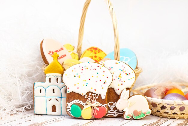 Feriado da Páscoa. Ovos coloridos em uma cesta. Coelhinho da Páscoa no sanduíche. Biscoitos de gengibre de Páscoa em forma de ovos e um templo. em um fundo claro de madeira.