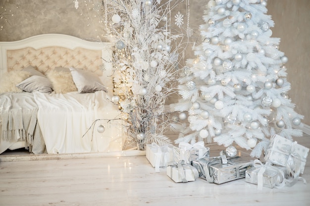 Feriado de ano novo, humor, interior minimalista elegante de ano novo, presentes e presentes embrulhados sob a árvore de Natal. grande quarto branco com cama branca