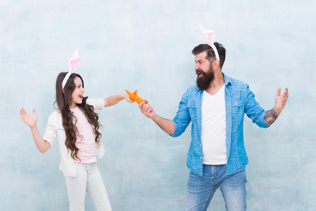 Feriado de primavera comemore a páscoa juntos cozinhar comida de páscoa hábitos saudáveis orelhas de coelho da menina e do pai família feliz usa orelhas de coelho diversão e felicidade da páscoa pai e filha brincam com cenouras