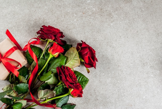 Feriado, dia dos namorados. Buquê de rosas vermelhas, gravata com uma fita vermelha, com caixa de presente embrulhada e vela vermelha. Em uma mesa de pedra cinza, vista superior