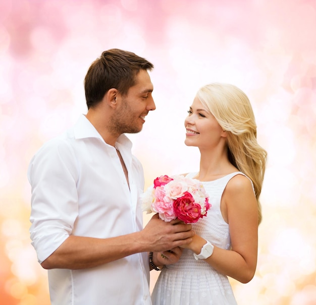 Feriados, amor, pessoas e conceito de namoro - casal feliz com um monte de flores sobre fundo de luzes rosa