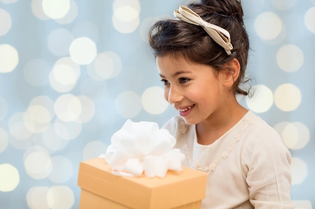 feriados, crianças, natal, pessoas e conceito de aniversário - menina feliz com caixa de presente sobre fundo de luzes