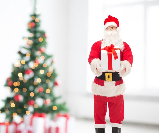 feriados e conceito de pessoas - homem fantasiado de papai noel com caixa de presente sobre sala de estar e fundo de árvore de natal