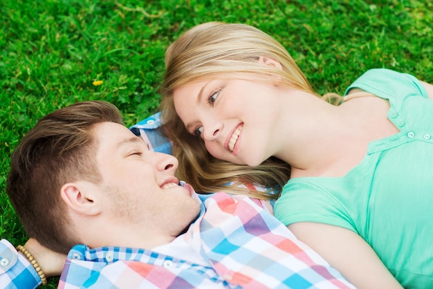 feriados, férias, conceito de amor e amizade - casal sorridente deitado na grama no parque