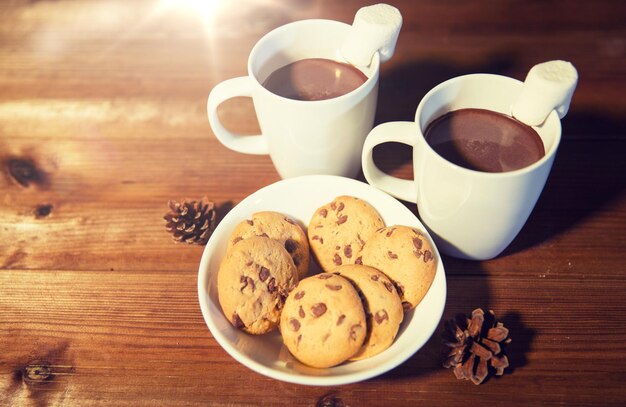 feriados, natal, inverno, conceito de alimentos e bebidas - close-up de xícaras com chocolate quente ou bebidas de cacau e marshmallow com biscoitos de aveia na mesa de madeira
