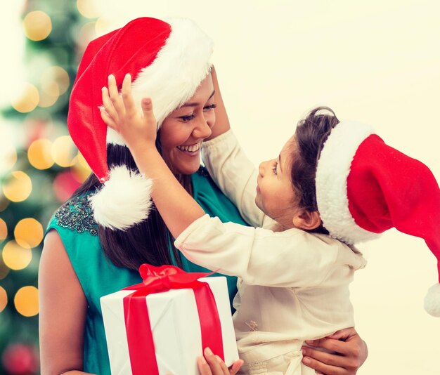 feriados, presentes, natal, conceito de natal - feliz menina mãe e criança com chapéus de ajudante de Papai Noel com caixa de presente