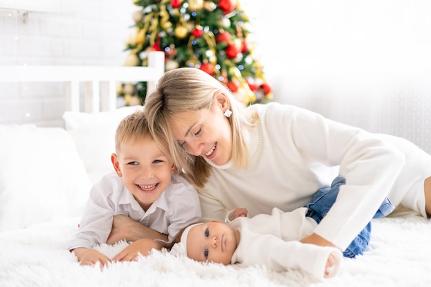 Férias de ano novo criança e bebê com uma jovem e linda mãe em casa celebram o Ch com a árvore de Natal