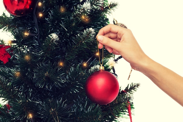 Férias de inverno, celebração e conceito de pessoas - close-up de uma mulher decorando a árvore de Natal com uma bola