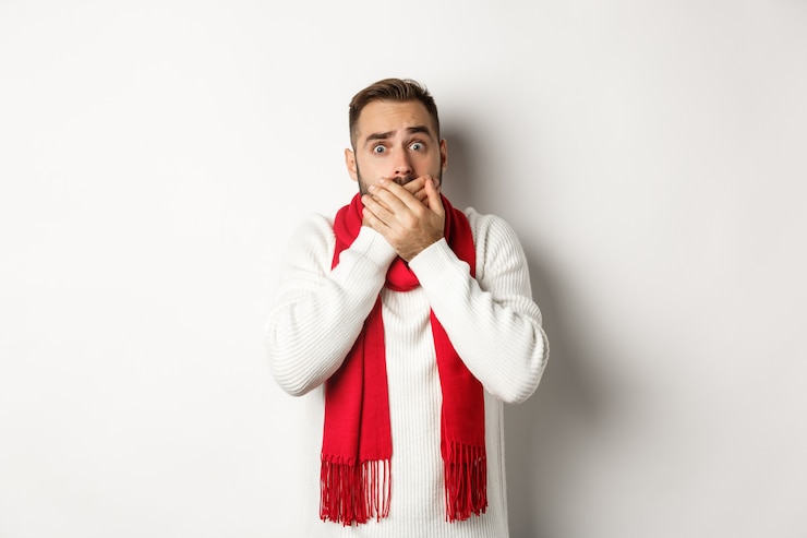 Foto férias de inverno e conceito de compras. homem assustado ofegando, tapando a boca e tentando não gritar, de pé assustado contra um fundo branco