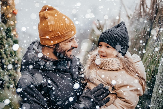 Férias de inverno e conceito de pessoas feliz pai e filha escolhendo árvore de natal no mercado de rua Escolhendo e comprando uma árvore de natal no mercado de natal