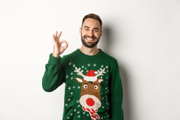 Férias de inverno e natal. Homem barbudo feliz mostrando sinal de ok e sorrindo, aprovo ou concordo, elogiando algo bom, em pé sobre um fundo branco