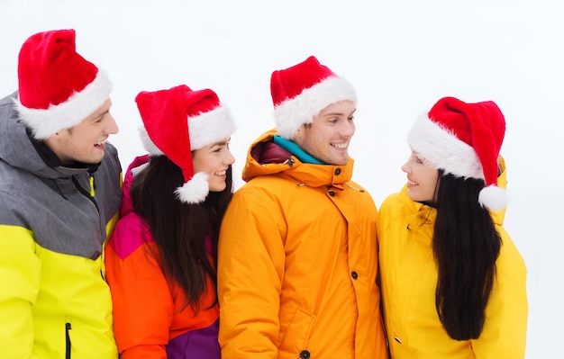 férias de inverno, natal, amizade e conceito de pessoas - amigos felizes em chapéus de papai noel e roupas de esqui ao ar livre