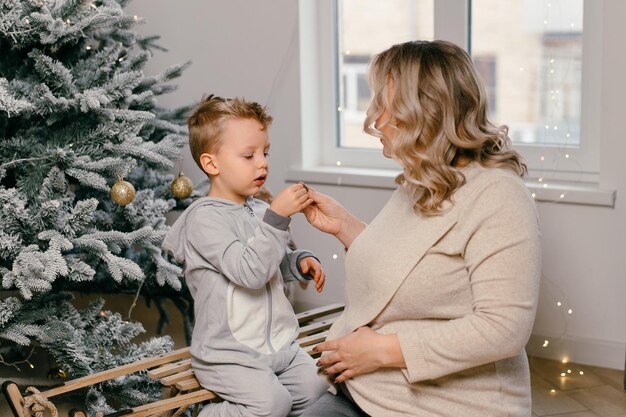 Férias de Natal caucasiana mãe brincando com filho fofo perto da árvore decorada do ano novo em casa Tradição familiar