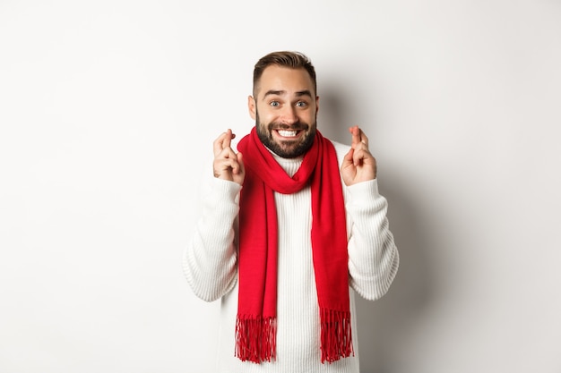 Férias de Natal e o conceito de ano novo. Esperançoso homem fazendo desejo com os dedos cruzados, esperando por presentes, em pé sobre um fundo branco.