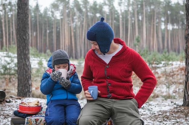 Férias de Natal, pai e filho bebendo uma bebida quente de ano novo. Família feliz em uma caminhada ao ar livre na floresta ensolarada de inverno