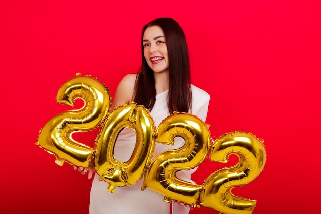 Férias de Natal - Uma jovem com um vestido branco segura os números 2022 em um fundo vermelho