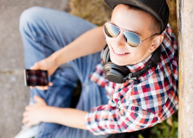 férias de verão, adolescente e conceito de tecnologia - adolescente com fones de ouvido e smartphone do lado de fora