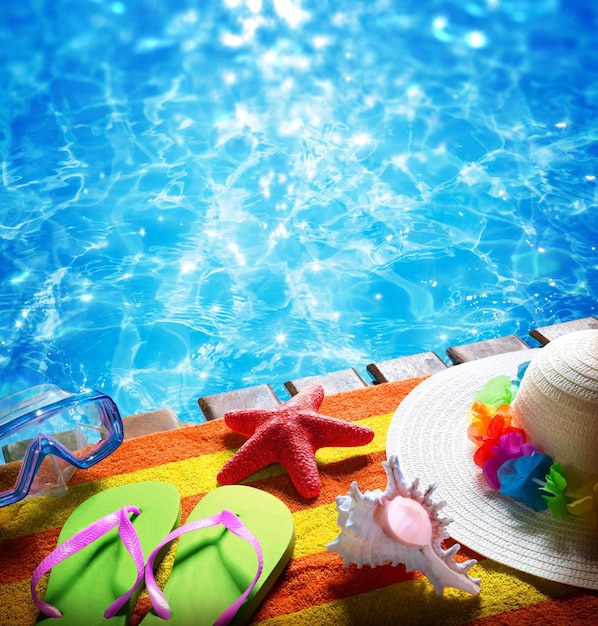 Foto férias de verão com toalhas, piscina, sandálias, chapéu e estrelas-do-mar.