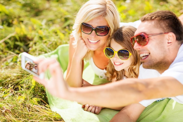 férias de verão, crianças e conceito de pessoas - família feliz com câmera, céu azul e grama verde tirando foto