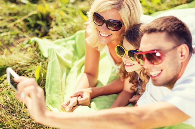 férias de verão, crianças e conceito de pessoas - família feliz com câmera, céu azul e grama verde tirando foto