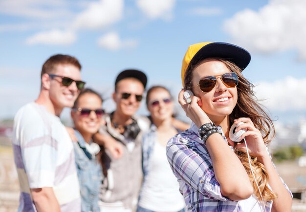 férias de verão e conceito adolescente - adolescente em óculos de sol, boné e fones de ouvido saindo com amigos do lado de fora