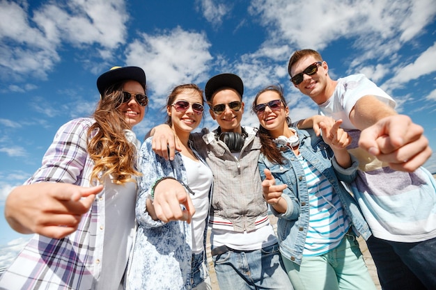 férias de verão e conceito adolescente - grupo de adolescentes sorridentes em óculos de sol pendurados do lado de fora apontando o dedo para você