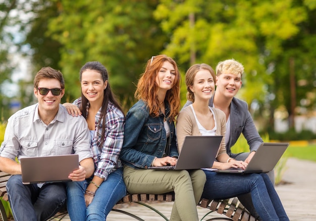 férias de verão, educação, campus, tecnologia e conceito adolescente - grupo de estudantes ou adolescentes com computador portátil